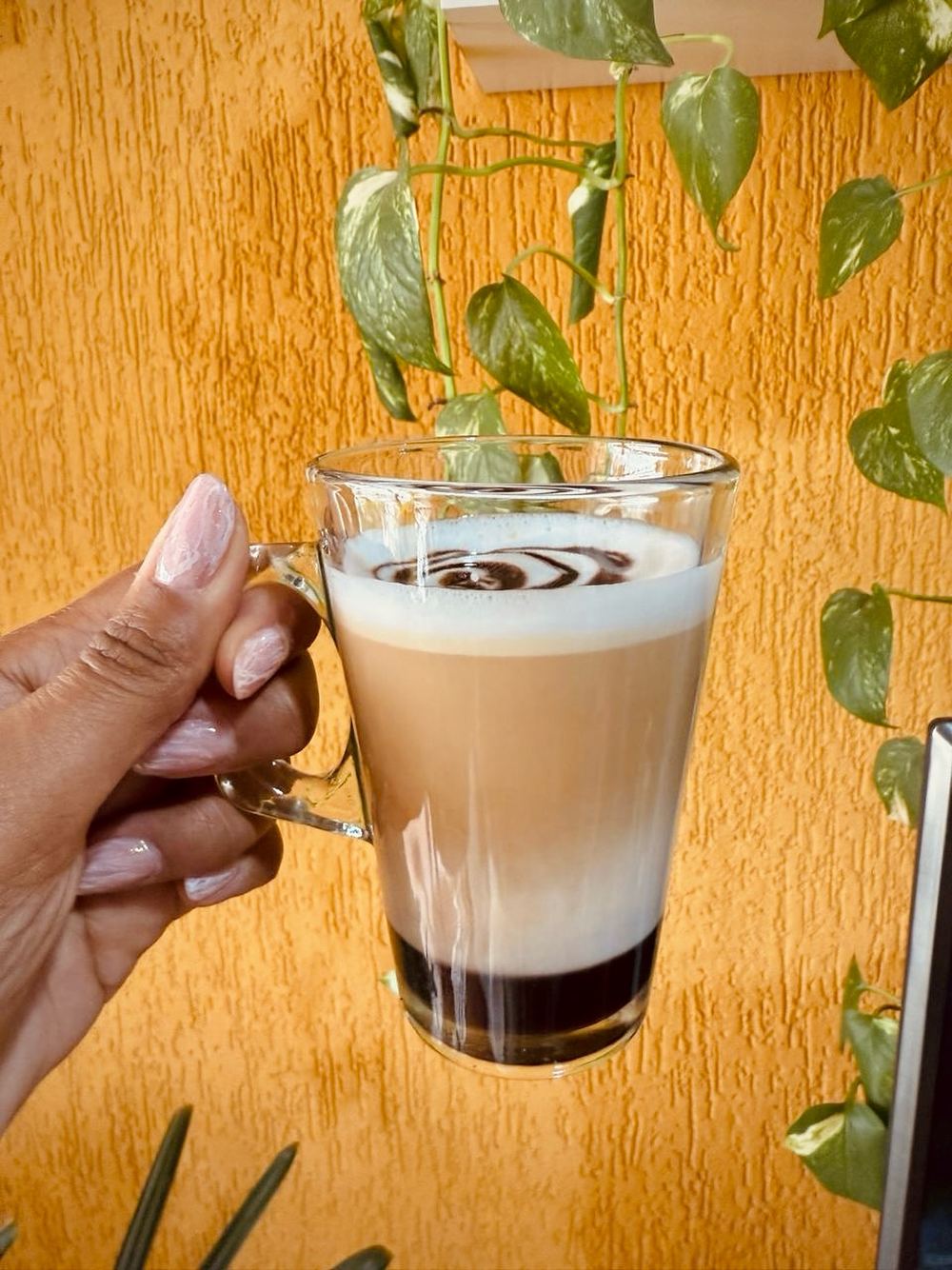 Mão segurando um latte em copo de vidro